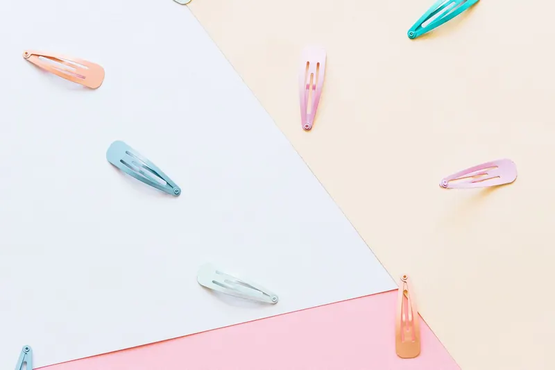 An artistic flat lay featuring colorful hair clips on a pastel geometric background