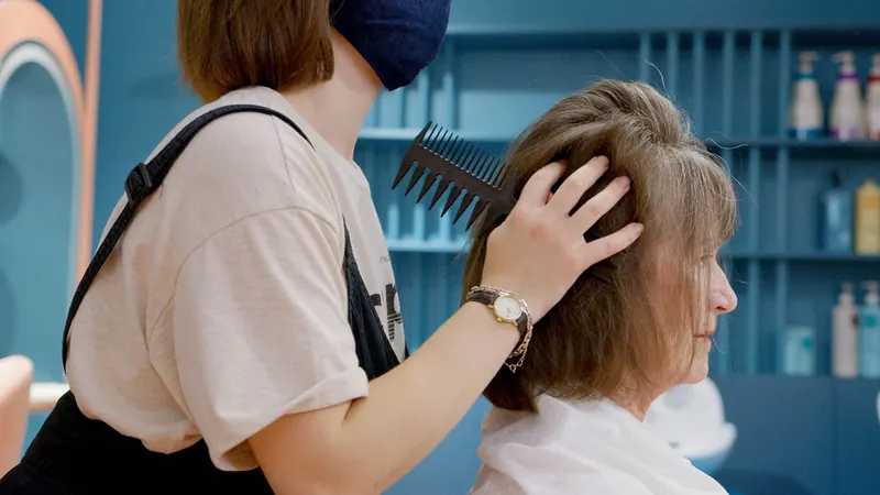 A hairstylist combing a senior woman's hair at an indoor salon, showcasing professional care