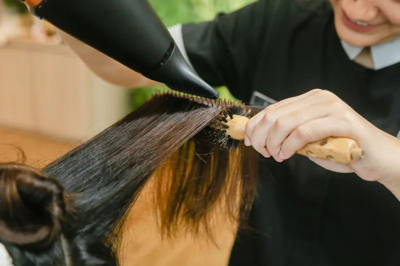 Close-up of hair stylist using a hairdryer and brush to style long hair