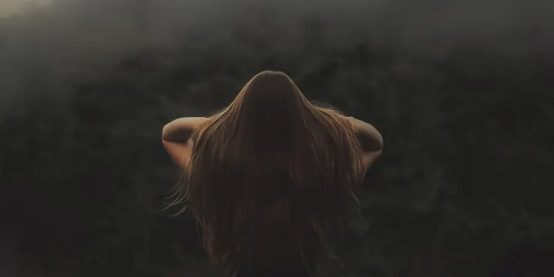 Back view of a woman with long hair, standing in a misty forest