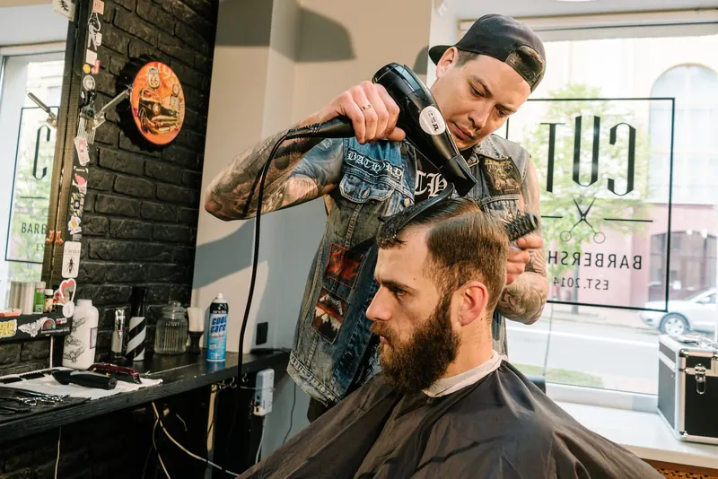 A barber uses a blow dryer to style a client's hair in a trendy barbershop setting