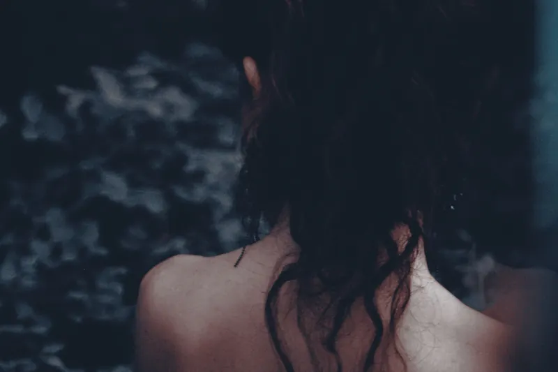 Artistic portrait of a woman seen from behind, highlighting her hair and bare shoulders in a moody setting