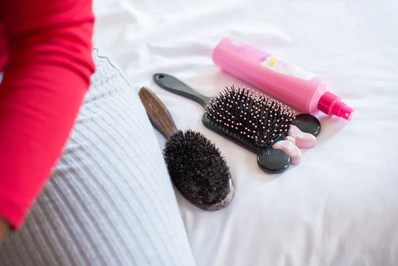 Close-up of hair styling tools including brushes and a pink spray bottle on white fabric