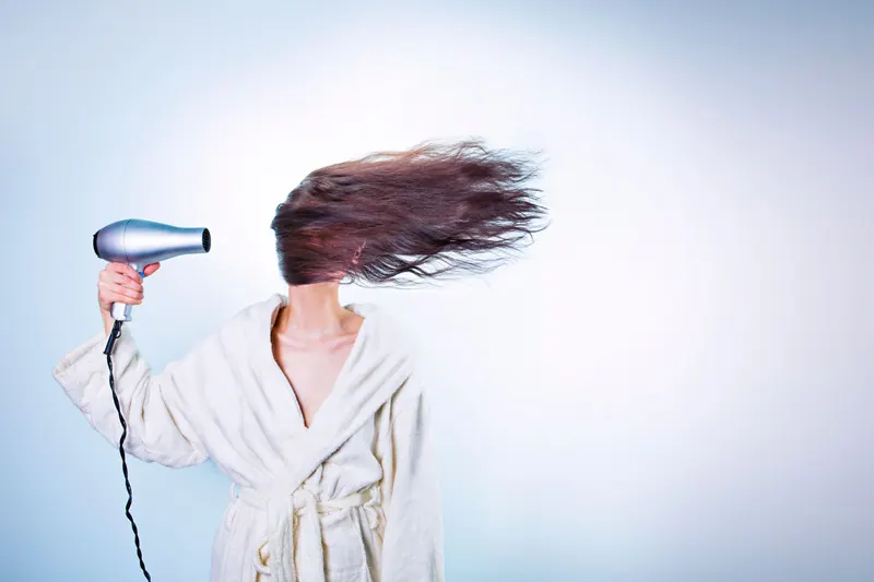 Woman in a bathrobe using a hairdryer, hair flying wildly. Indoor setting