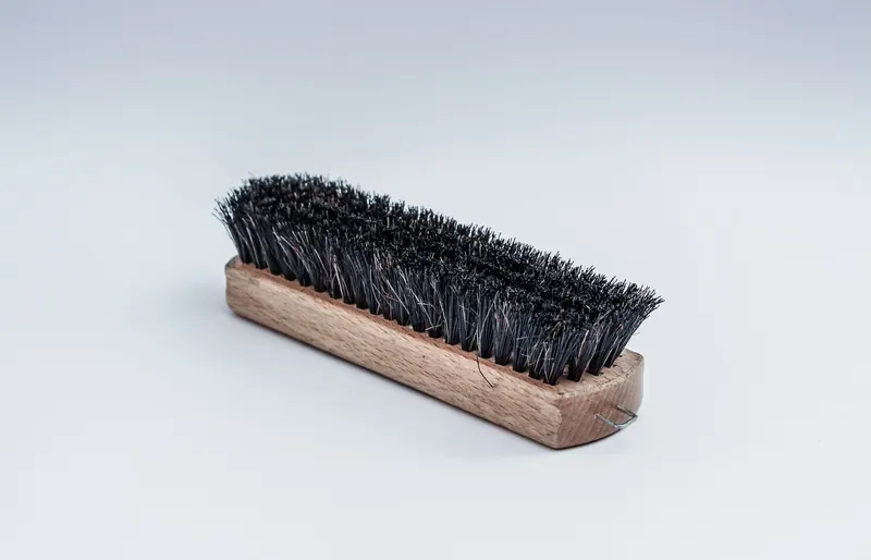 Close-up of a wooden cleaning brush with dense black bristles on a white background