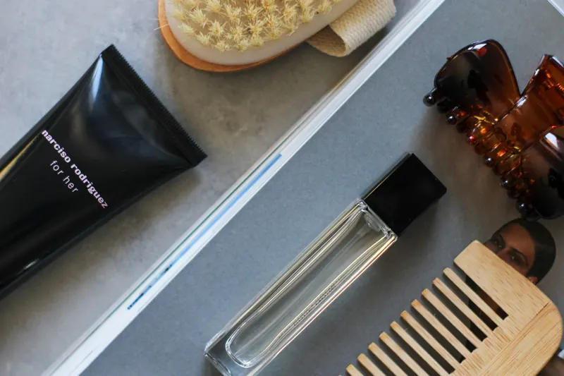 Stylish flat lay of beauty essentials including comb, brush, hair clip, perfume, and body lotion